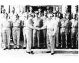Black and white photo of two men shaking hands with other uniformed men in background