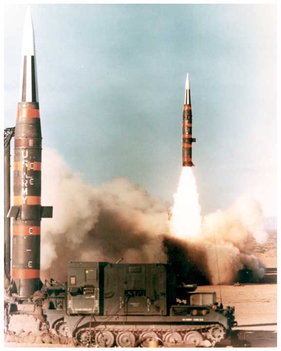 Photo of 2 Pershing missiles, one upright in launch position, the other being launched.