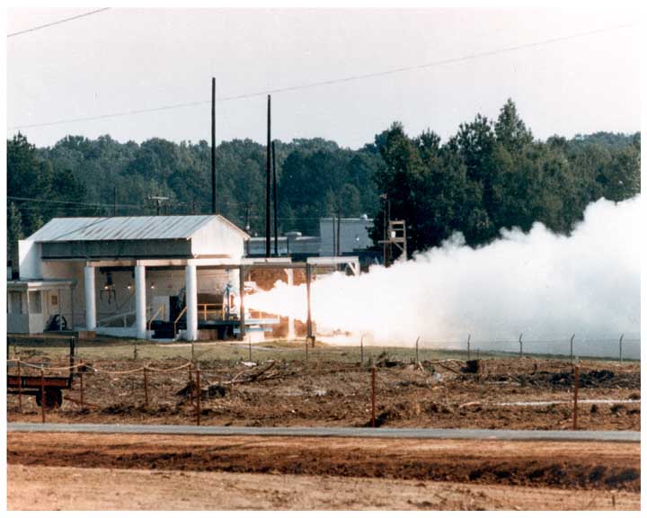 Photo of a Pershing missile on its side mounted in a test stand with rocket being fired, plume of exhaust exiting test stand sideways