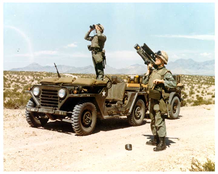 Photo of a soldier with a REDEYE missile launcher, with another soldier in the background standing atop a 1/4 ton JEEP looking through binoculars.