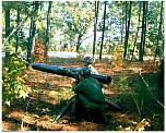 Photo of 2 soldiers employing a ground mounted TOW missile in a wooded area.