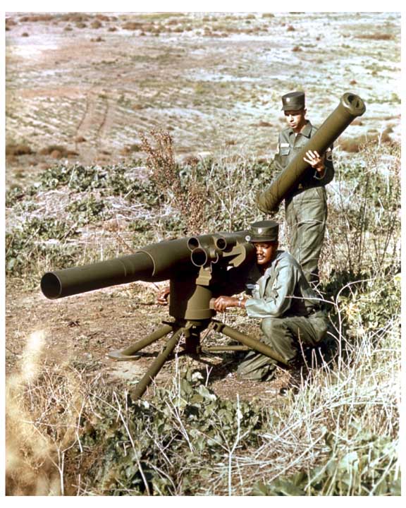 Photo of a soldier sighting in a ground mounted TOW missile, with another soldier behind him holding a missile.