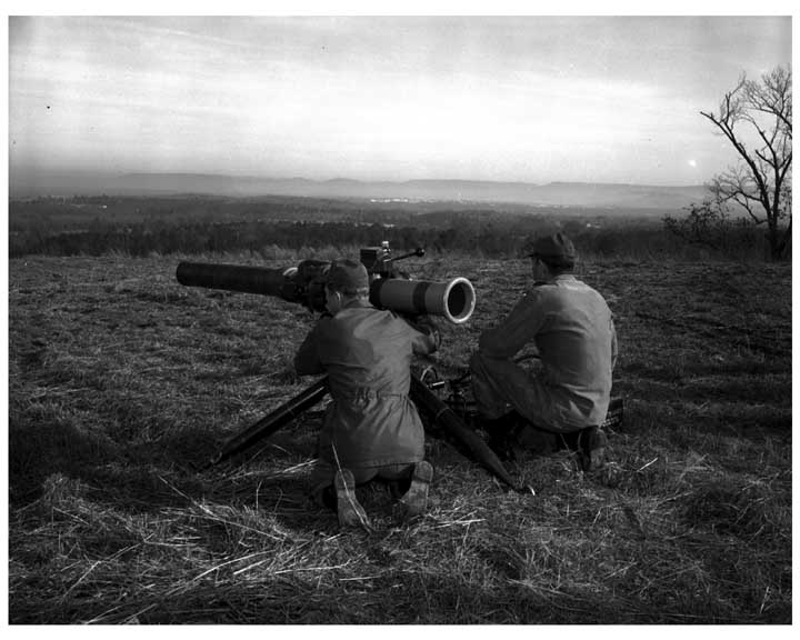 Photo of 2 soldiers kneeling next to a ground mounted TOW missile system, with one soldier sighting in the weapon.