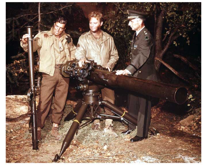 Photo of an Army private and a sergeant showing an Army officer a recoiless rifle and a ground mounted TOW missile system.  The soldiers are in field uniforms, while the officer is in class A dress uniform.