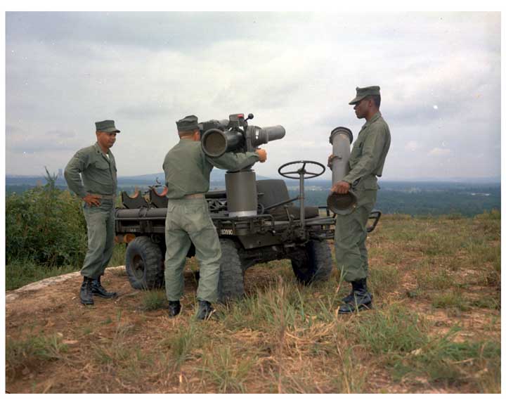 Photo of 3 soldiers standing with a TOW missile system mounted on a M274 Mechanical Mule.  One soldier is sighting the weapon, while another solider is holding a missile in preparation for reloading.